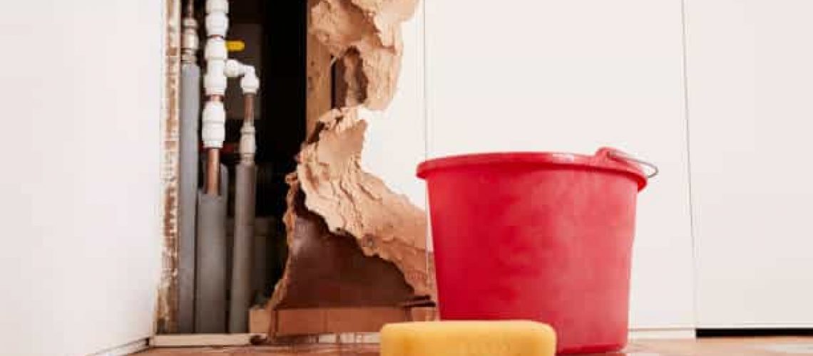 Damaged wall, exposed burst water pipes, sponge and bucket